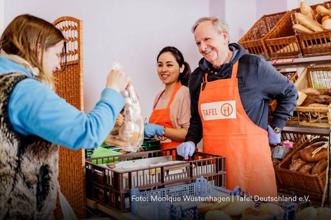 Frau bekommt Brot gereicht an einem Stand mit zwei Freiwilligen der Tafel